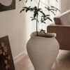 The florentina white floor vase in XL on a living room floor with a plant