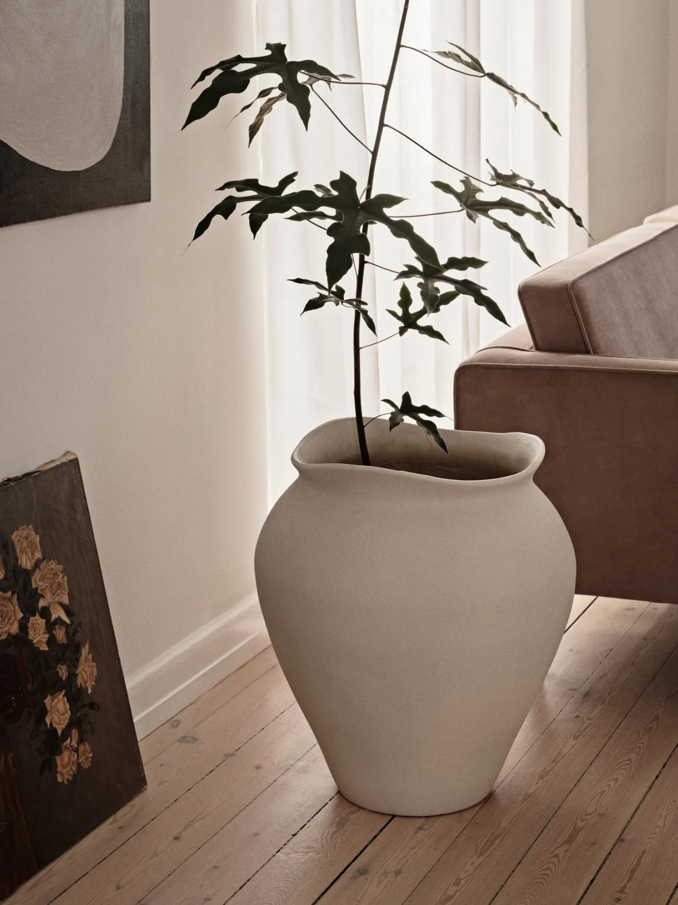 The florentina white floor vase in XL on a living room floor with a plant