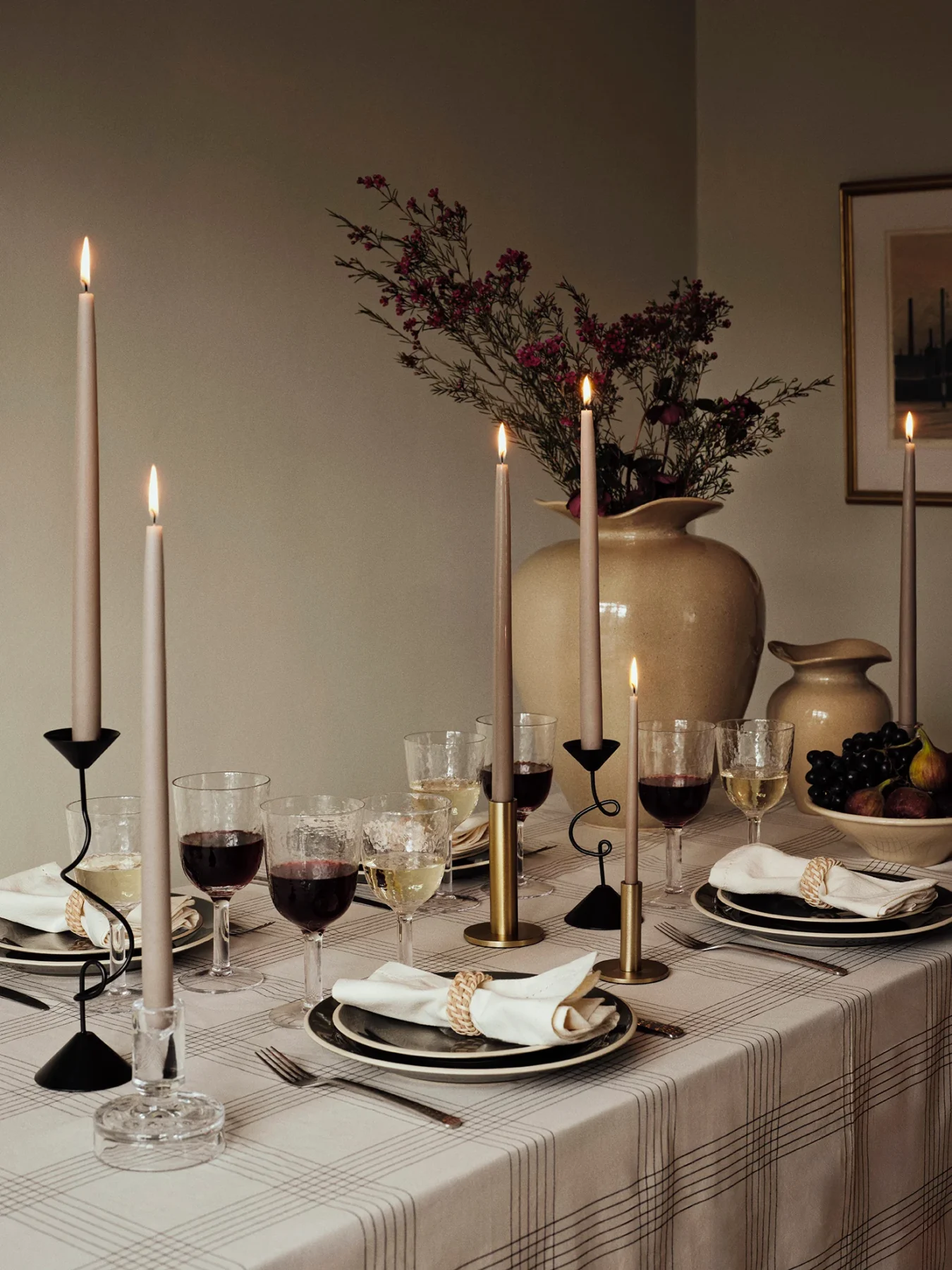 Large beige florentina vase with flowers on a table set for dinner with candles lighting
