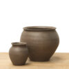 Medium brown ceramic vase with a rounded shape, flared rim, and earthy finish on a wooden surface.