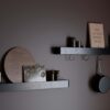 Protopia wall shelf in black stained ash veneer with a slim profile and curved ends, ideal for displaying books, artwork, photographs, and decorative accessories in modern interiors.