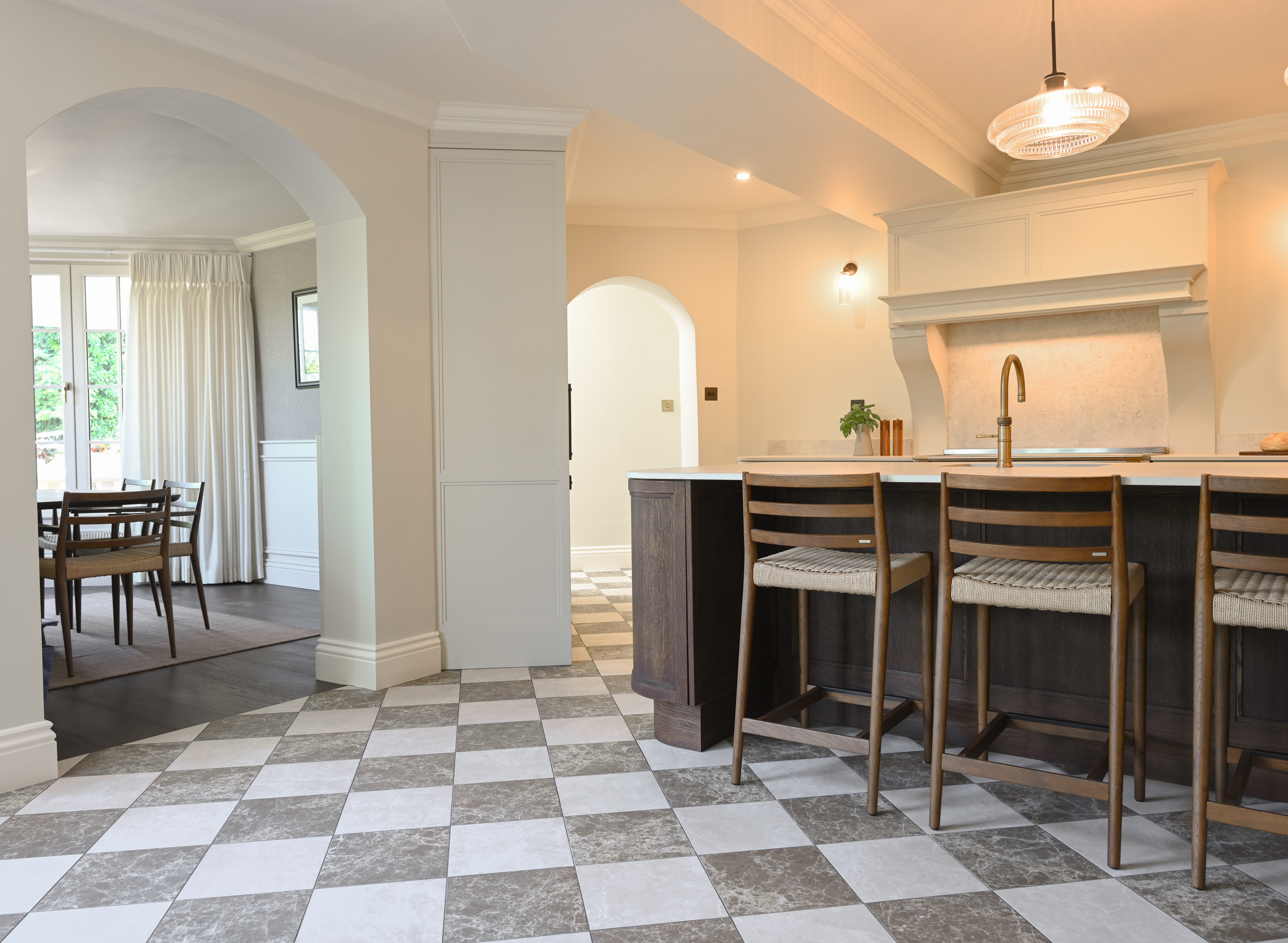 Open-plan two-tone kitchen with a dark-stained island, woven bar stools, arched openings and checkerboard flooring.