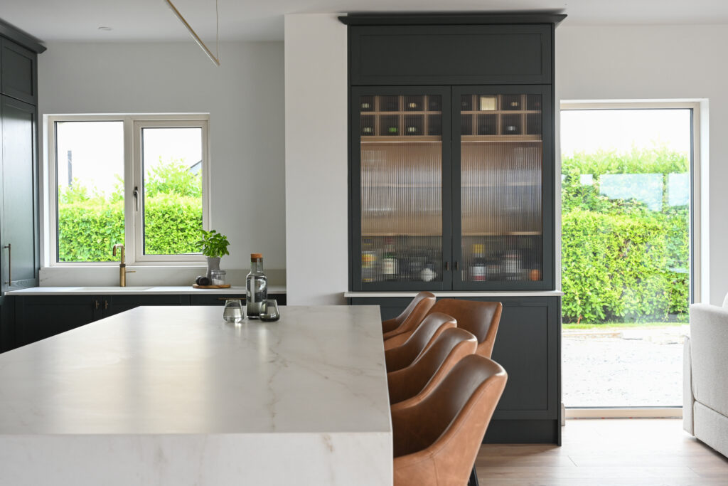 Bespoke kitchen island with Dekton Rem worktop and deep forest green bar cabinet in an open-plan kitchen extension