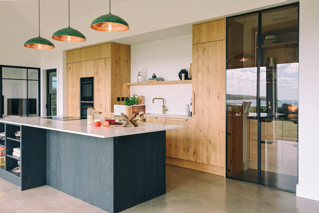 Bespoke oak kitchen cabinetry with integrated ovens, Quooker tap, open shelf and light stone worktop.