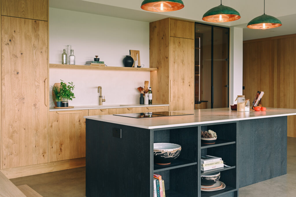 Bespoke oak kitchen with contrasting dark island, integrated hob, open shelving and statement pendant lights.